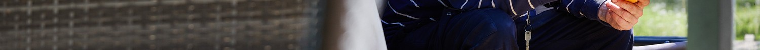 Ein Mann im blauen Pullover sitzt in einer Hollywoodschaukel und liest in einem Buch mit gelben Umschlag