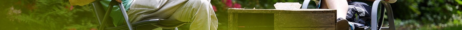 Zwei Männer sitzen auf einem Stuhl im sommerlich grünen Garten und unterhalten sich.