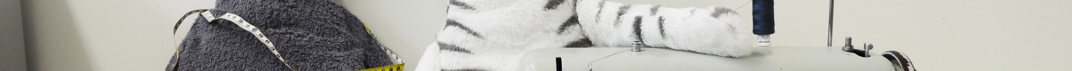 Zwei handgefertigte Plüschkatzen, einmal in grau und in schwarz-weiß, sitzen neben einer grauen Nahmaschine.