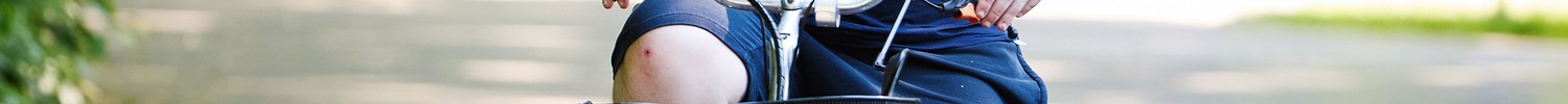 Ein Mann in blauer Kleidung fährt auf einem grauen Weg auf einem Fahrrad im Hintergrund grüne Bäume.